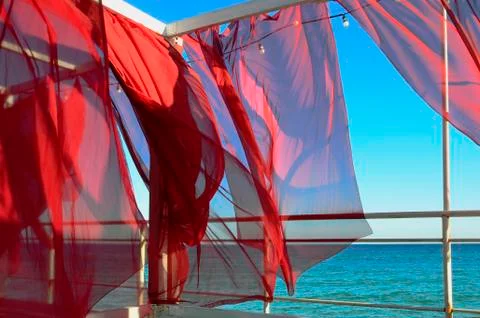 Red curtains develop in the wind against the background of the sea 스톡 사진