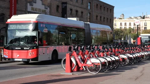 Red cycles parked in a row for rent city buses pass by near Palau De Mar Stock Footage 171770418
