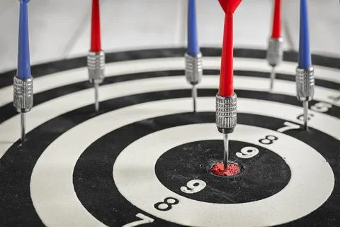 Red dart arrow hitting in the target center of dartboard Stock Photos