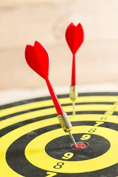 Red dart arrow hitting in the target center of dartboard Stock Photos