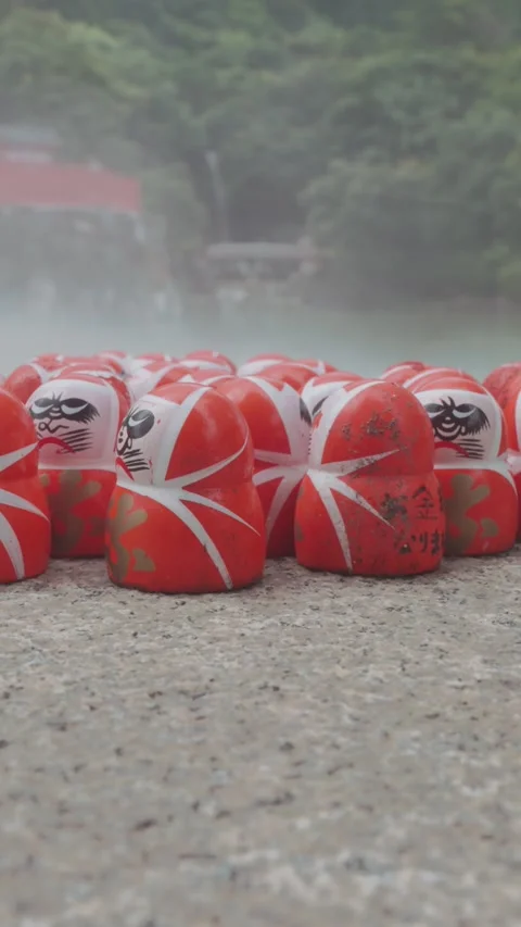 Red Daruma dolls rest on stone platform at Katsuoji Temple in Osaka, surrounded Stock Footage 345741160