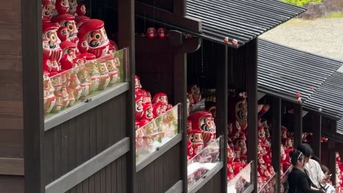 Red Daruma lucky dolls displayed on wooden ledges at Katsuo-ji Temple in Minoh Stock Footage 344554660