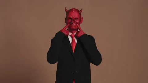 Red devil businessman forcing a smile on brown background Stock Footage 296240600
