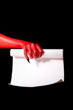 Red devil hand with black nails holding paper scroll Foto stock