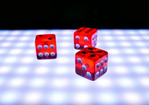 Red dice on a luminous surface on a black background, concept of board games Stock Photos