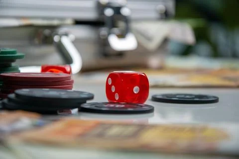 A red dice sits on a table with black and red chips, a stack of playing cards Foto stock