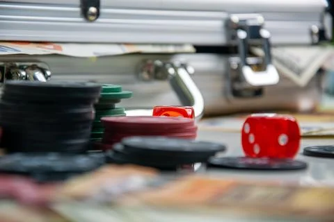 A red die and poker chips sit on a table beside a metal case Stock Photos
