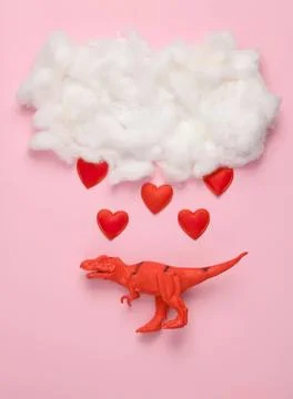 Red dinosaur toy under a cloud with hearts on pink background 스톡 사진