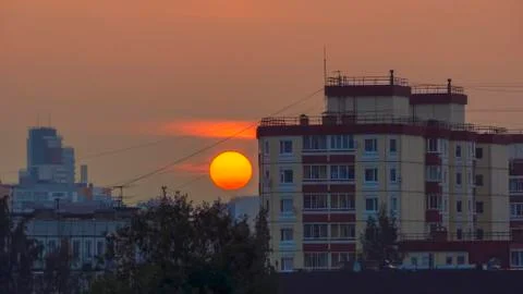 Red disk of the sun at sunset on a background of tall buildings of city 스톡 사진