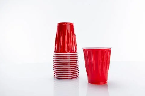 Red disposable plastic cup put next to a horizontal stack of cups against a whit 库存照片