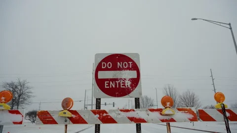 A red Do Not Enter sign stands behind road closure barriers during snowy winter Stock Footage 327567532