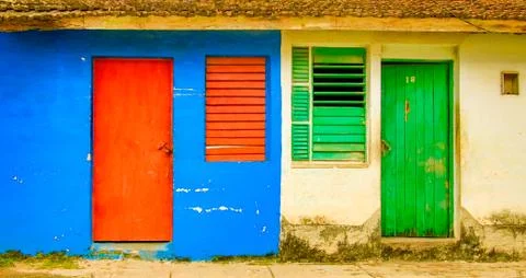 Red door &amp; window on blue wall neighbors green door and window on yellow wall Stock Photos