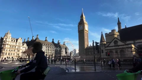A red double decker bus drives past the Houses of Parliament and Big Ben in Vídeos de archivo 328353099