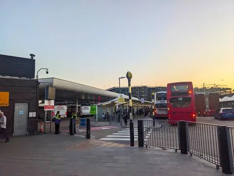 Red double-decker bus at Heathrows busy central bus station against a golden Fotos de archivo