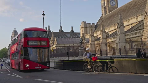 A red double decker city bus, Wandsworth 87, along with cyclists, and scooters Stock Footage 257744650