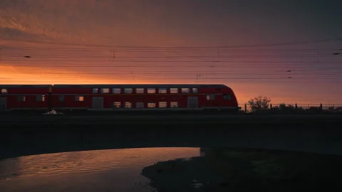 Red double-decker train passing over a bridge at vibrant sunset Stock Footage 315172708