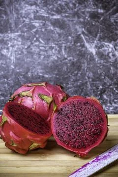 Red dragon fruit cut in half on top of a board with a white knife. Photos