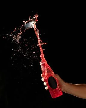 Red drink splash on black background. Backlit Male hand holding transparent Stock Photos