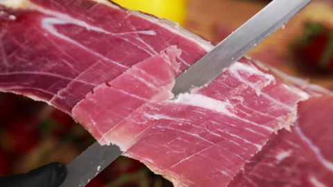 Red dry-cured prosciutto with some fat lines being sliced with sharp knife Video stock 270004265