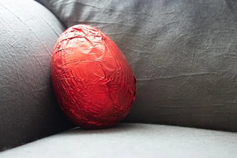 Red easter egg on the corner of a couch still unwrapped Stock-Fotos