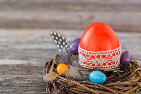 Red Easter egg decorated with lace in small nest on wooden background Foto stock