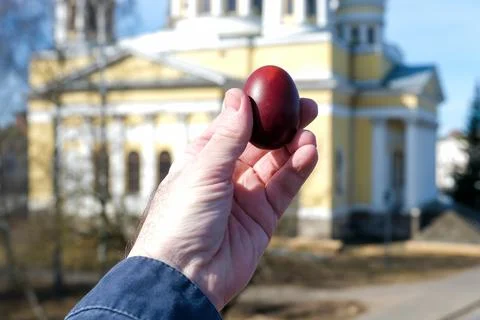 Red Easter egg held in hand against a soft blurred church background. Symbol  Photos
