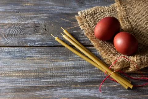 Red easter eggs and beeswax candles on burlap over rustic wooden table for Stock Photos
