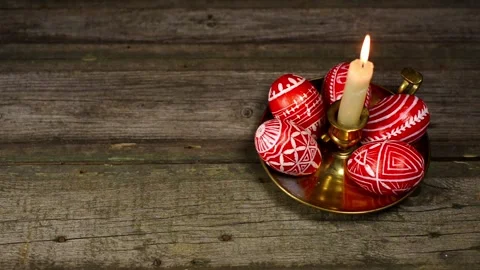 Red easter eggs with folk pattern on brass candlestick on wood. Man put one egg Stock Footage 127886664