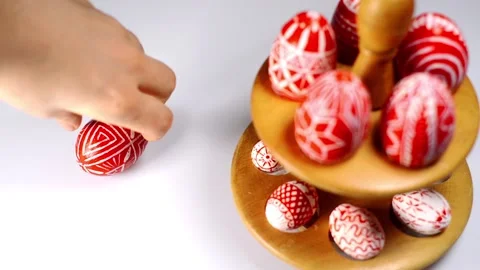 Red easter eggs with folk pattern lay on wooden stand for eggs. Man rotate egg Stock-Footage 127886749