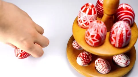 Red easter eggs with folk pattern lay on wooden stand for eggs. Man rotate egg Stock Footage 127886797