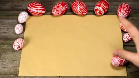 Red easter eggs with folk pattern lay on edge of sheet of paper. Man rotate egg Stock-Footage 127887094