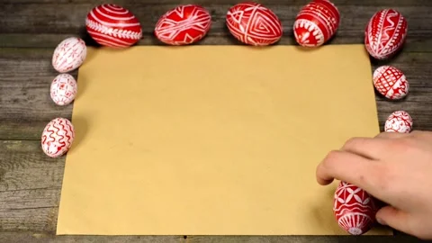 Red easter eggs with folk pattern lay on edge of sheet of paper. Man rotate egg Video stock 127887098
