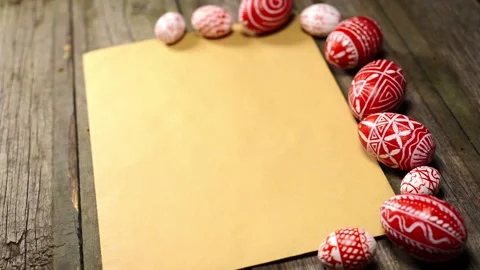 Red easter eggs with folk pattern lay on edge of sheet of paper. Man rotate egg Video stock 127887144