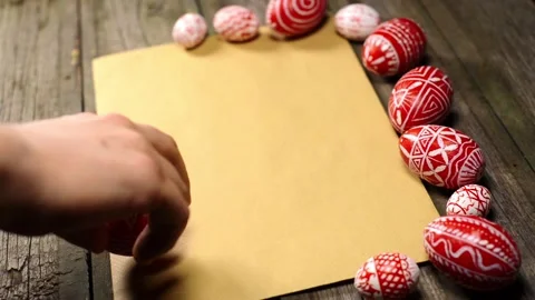 Red easter eggs with folk pattern lay on sheet of paper. Man's hand rotate egg Stock Footage 127887169