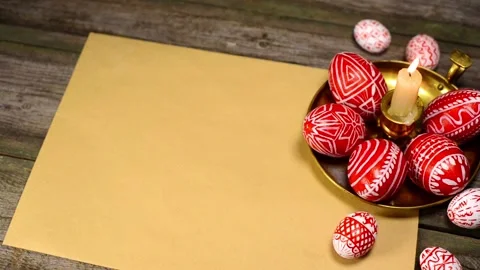 Red easter eggs with folk pattern lay on candlestick on. Man's hand rotate egg. Stock-Footage 127887384