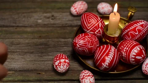 Red easter eggs with folk pattern lay around brass candlestick. Man rotate egg Video stock 127887525