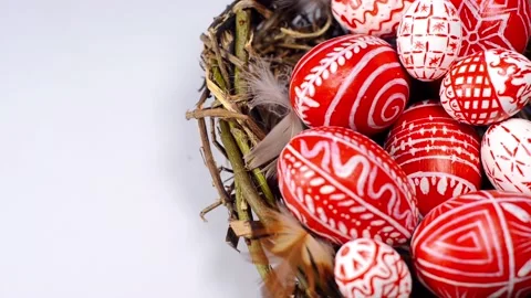 Red easter eggs with folk pattern inside nest on white. Man's hand rotate egg. Video stock 127887841