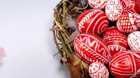 Red easter eggs with folk pattern inside nest on white. Man's hand rotate egg Stock Footage 127887862