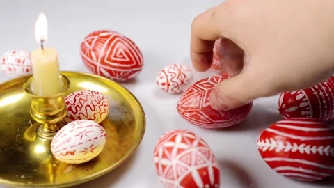 Red easter eggs with folk pattern lay around and on candlestick. Man rotate egg Stock-Footage 127888564