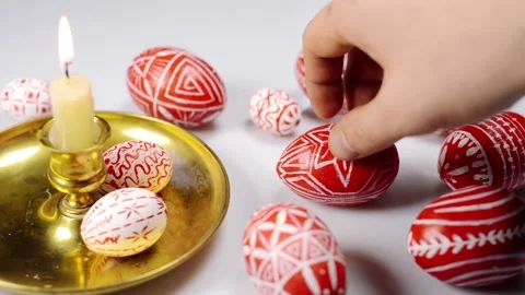 Red easter eggs with folk pattern lay around and on candlestick. Man rotate egg Stock Footage 127888602