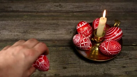 Red easter eggs with folk white pattern lay on candlestick. Man rotate egg Video stock 127886644