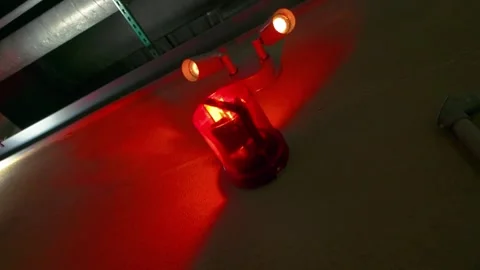 Red emergency light illuminating a dim industrial setting with overhead pipes Stock Footage 324039579