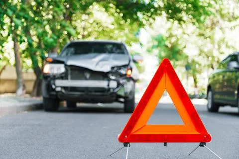 Red emergency stop triangle sign on road during a car accident. Broken gray car Stock Photos