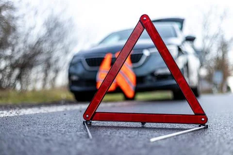 Red emergency warning triangle placed on road near a broken down car Fotos de archivo