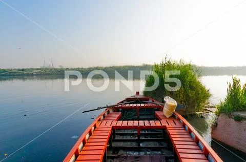 Red empty boat moored near some bushes on a blue serene river Stock Photos