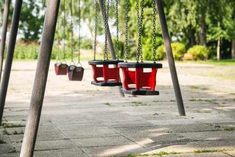 Red empty chain swing in playground on a blurred background, close up. Stock Photos