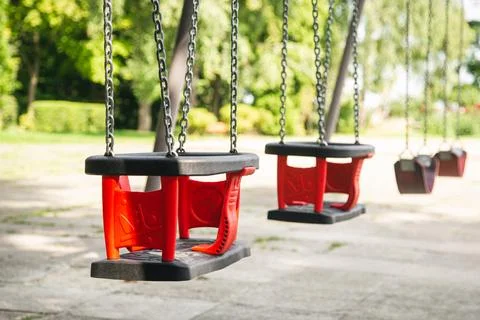 Red empty chain swing in playground on a blurred background, close up. Stock Photos