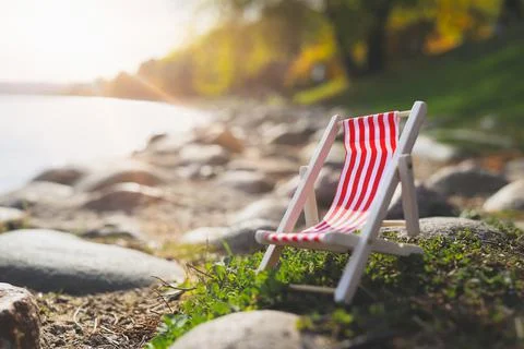 Red empty striped chaise longue on rocks by lake. Stock Photos