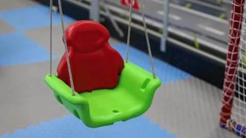 Red empty swing made of plastic in the children's center Video stock 220554246