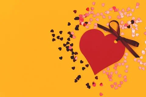 Red empty tag in a heart shape with tied ribbon bow and confetti. Stock Photos